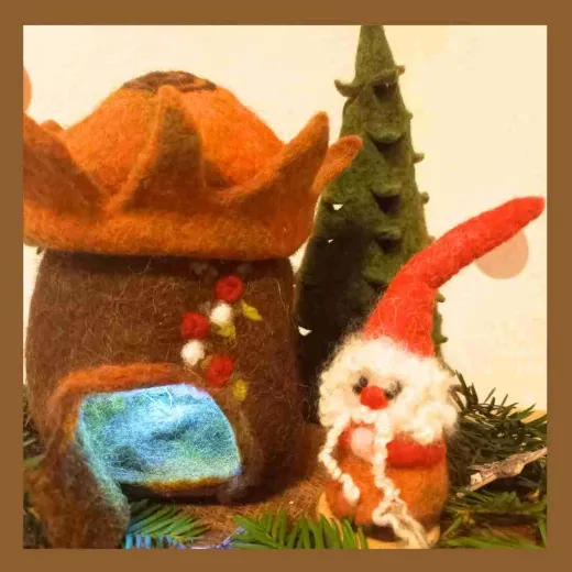 Foto eines handgefilzten Funkenhauses mit Krönchen-Dach, kleinem Tannenbaum und Funkenwichtel. Aufgenommen im Tageslicht, natürliche Farben, liebevolle Details. Zeigt das Ergebnis der Winterzauber-Filzanleitung.